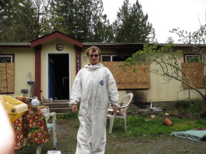 Matthew, suited up so he can work inside the house.  Smoke damage easily visible on the outside wall, door opens to nothing but blackness.  Inside, boxes filled with things that might be salvageable, furniture that we hoped to save and, it turns out, many things that we might have been able to recover had we only known which...   Taken April 9, on the day the professional cleaners came to grab what they had previously identified; far less than they could have.