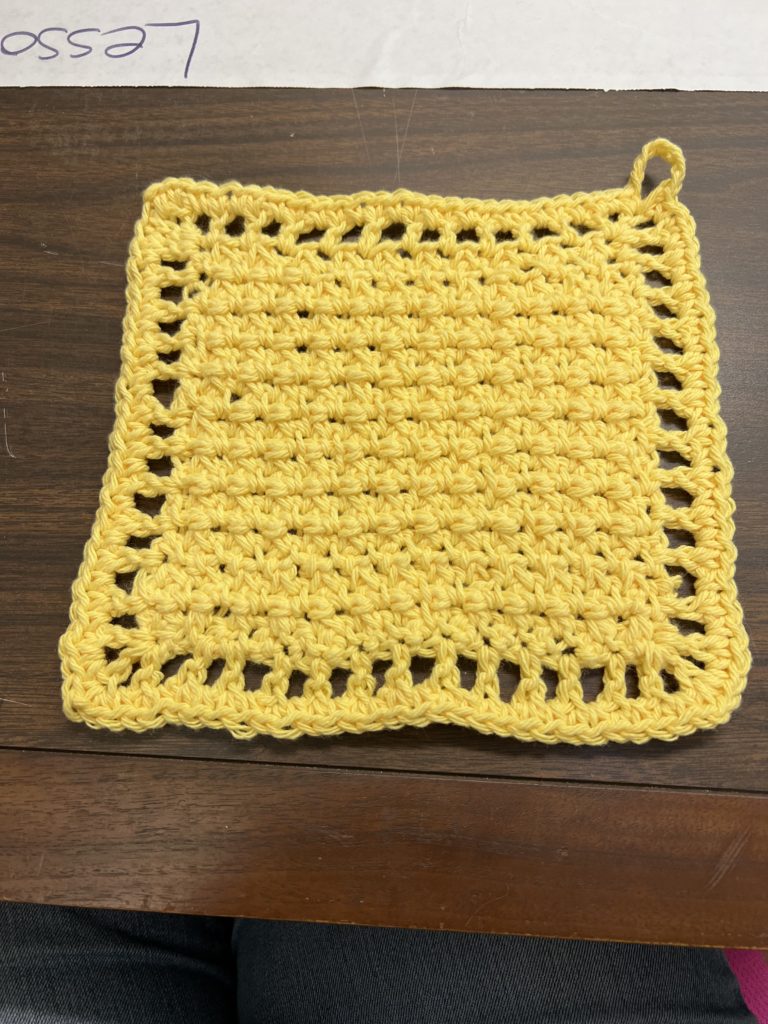 An all-yellow washcloth on a walnut desktop, with an open border and hanging loop.