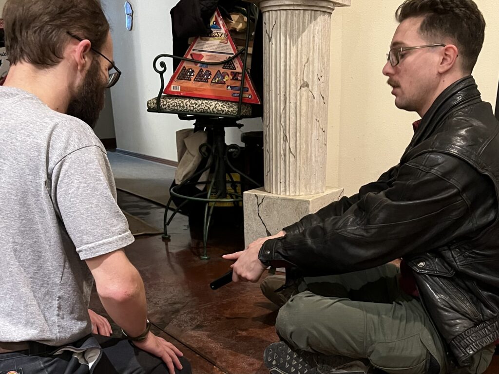 Two young men seated on floor discussing an object of interest.