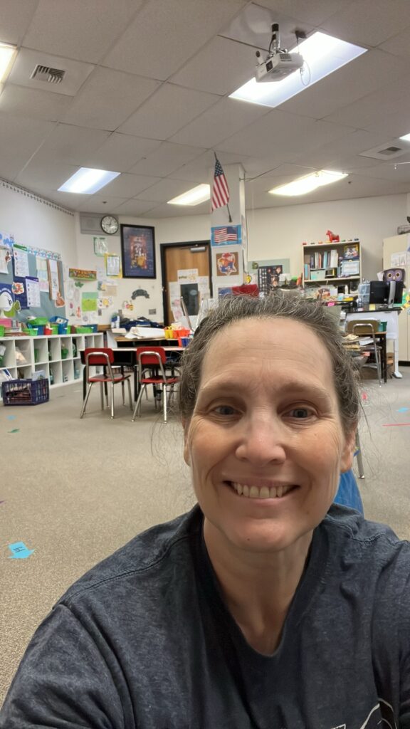 smiling face of person sitting on floor with a classroom in the middle of rearranging in the background